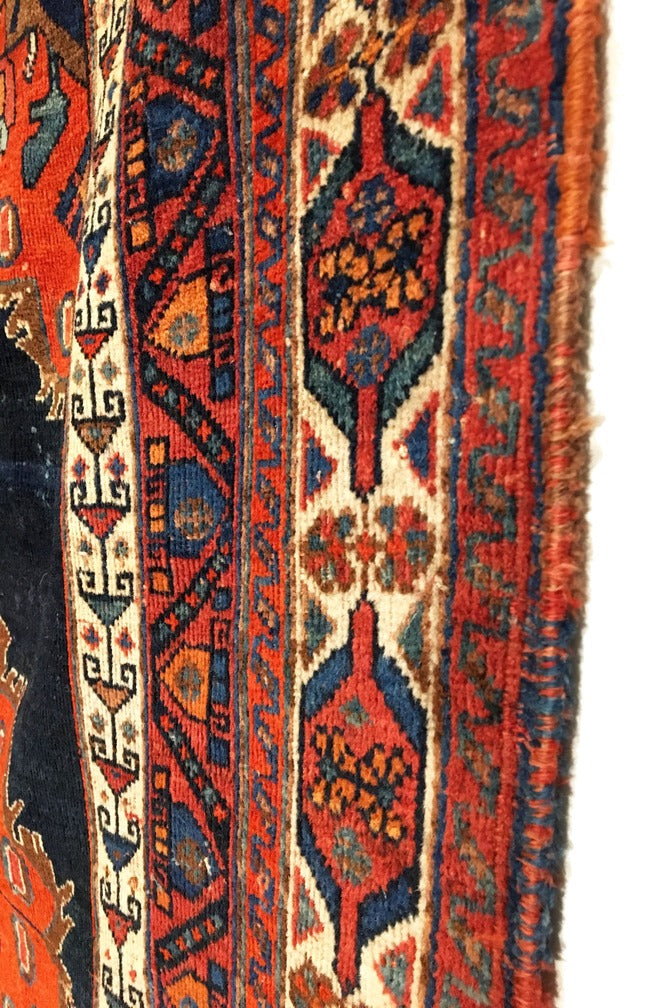 An antique Persian Afshar rug with a vibrant floral-patterned design in shades of red, blue, green, and beige, featuring a dark indigo field and decorative vases at the top and bottom.
